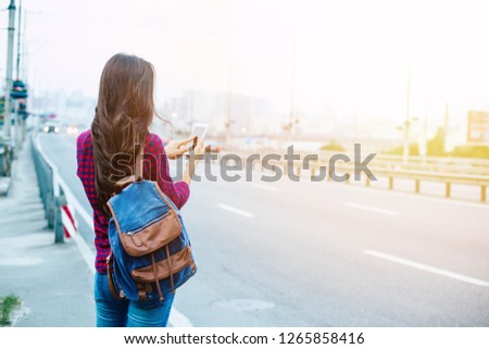 Beautiful young tourist woman with backpack and smart phone is standing on the road in new city and trying to search the right way