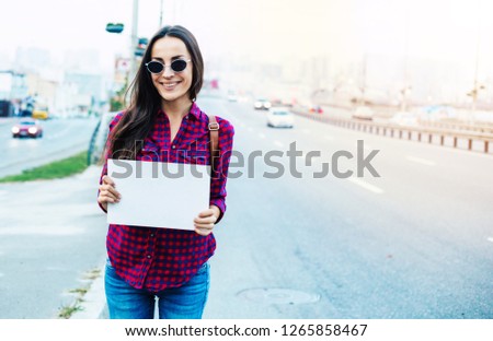 Beautiful young woman tourist or treveler with backpack to go hitchhiking at road with blank banner in hands