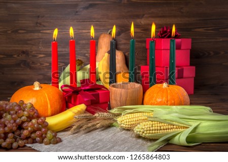 Kwanzaa holiday concept with candles red, black and green, gift box, pumpkins, ears of wheat, grapes, corns, banana, bowl and fruits on wooden background, close up