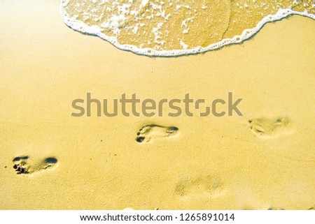 female foot steps on the beach sands with sea waves