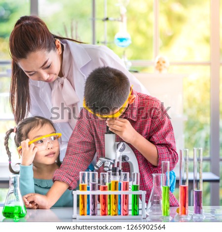 Science teacher teach Asian students in laboratory room, teacher look through microscope, colorful test tube and microscope on table , concept for study in laboratory room.