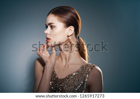 beautiful young woman in iron earrings and in a dress with sequins looks away on a gray background              