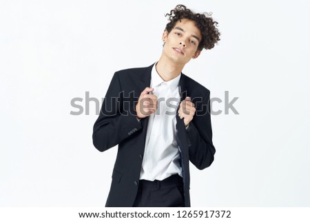 The guy with curly hair straightens his jacket on a light background               