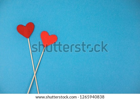 Two felt red and coral hearts on a blue background on wooden skewers.