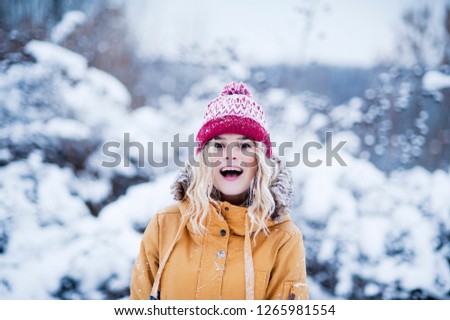 Very beautiful bright young girl in a red hat and yellow mittens on the background of a winter park in the snow. Winter holidays concept.