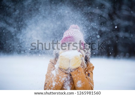 
Very beautiful bright young girl in a red hat and yellow mittens on the background of a winter park in the snow. Winter holidays concept. Throw and blow snow