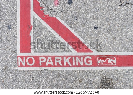 A red and white no parking sign, with lines, painted on concrete.