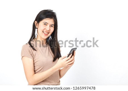 Asian Portrait of a smiling young woman holding mobile phone and looking up at copyspace isolated wall over grey background