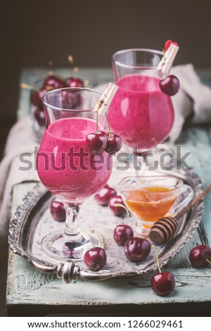 Healthy cherry smoothie with frozen strawberry, coconat water and honey in glass on white wooden table.