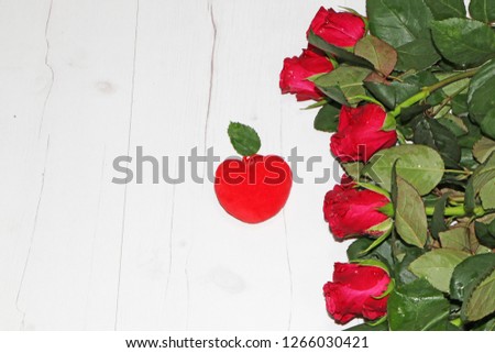 Red roses on wooden background. Nearby is a red heart.