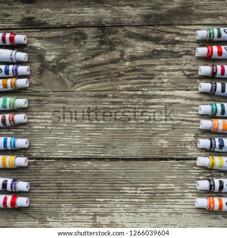 Paint tubes, brushes for painting and palette knifes on old wooden background.