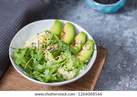 White bowl with couscous, sliced avocado and black sesame on the gray background