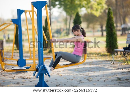 Young athletic girl is sitting on a sports simulator on a street playground in the autumn.
