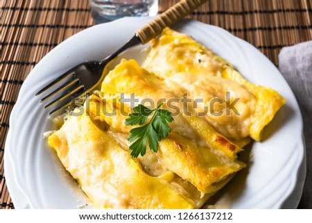 Homemade Italian Cannelloni with ricotta, spinach and bechamel sauce, with a basil leaf in a white plate and wooden background. Food photography