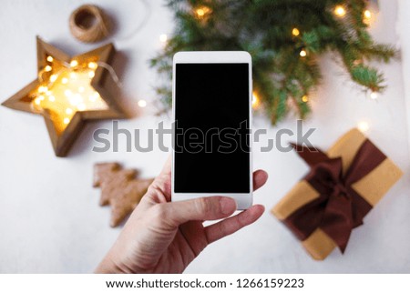 female hand with a phone takes pictures of New Year's decorations and fir branches.