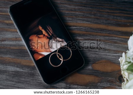 Golden wedding rings lie on a smartphone with newlyweds picture on a screen