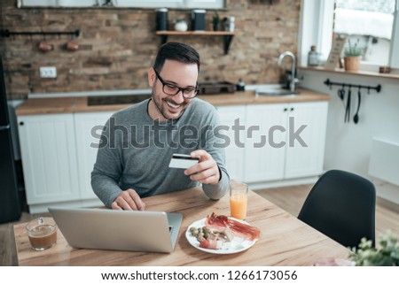 Young handsome man sitting at home with laptop and credit card.