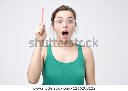Beautiful excited woman in eyeglasses and green t-shirt isolated on gray background. Excited student is inspired with a great idea.