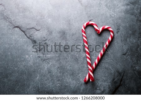 Christmas candy canes heart-shaped isolated on stone background. Holiday mood. Top view with text space