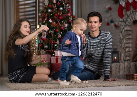 family sits with the baby sitting near the Christmas tree, the baby is one year old and a young woman and a man are waiting for Christmas