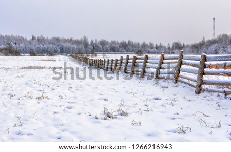 Snow-covered field in the countryside. A wooden fence of farmland. 