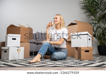 Photo of woman with champagne glass sitting on floor among cardboard boxes