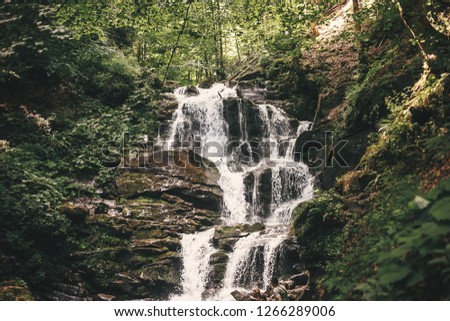 Beautiful waterfall in forest in mountains with cascade with flowing water. Beautiful outdoors scenery. Exploring waterfall in woods. Copy space.