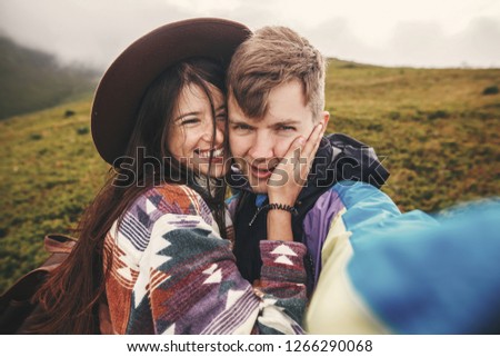 Happy hipster couple making selfie and smiling on top of  sunny  mountains. Stylish couple in love taking selfie photo and having fun. Travel together and Wanderlust concept.