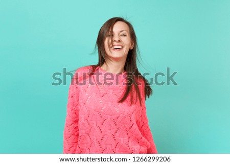 Joyful beautiful young woman in knitted pink sweater with fluttering hair isolated on blue turquoise wall background, studio portrait. People sincere emotions, lifestyle concept. Mock up copy space
