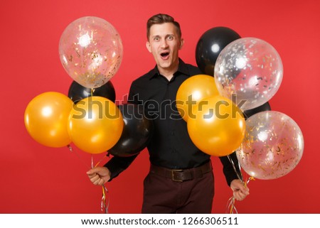 Excited young man in black classic shirt holding air balloons celebrating isolated on bright red background. Valentine's International Women's Day Happy New Year birthday mockup holiday party concept