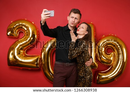 Couple guy girl in dress black shirt celebrating holiday party hold cellphone isolated on bright red wall background golden numbers air balloons studio portrait. Happy New Year 2019 Christmas concept
