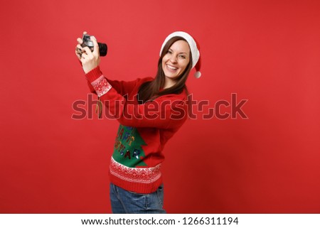 Pretty young Santa girl in Christmas hat doing taking selfie shot on retro vintage photo camera isolated on red background. Happy New Year 2019 celebration holiday party concept. Mock up copy space