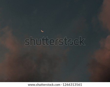 Small crescent moon in golden tone, surrounded by clouds at dusk, sao paulo, Brazil