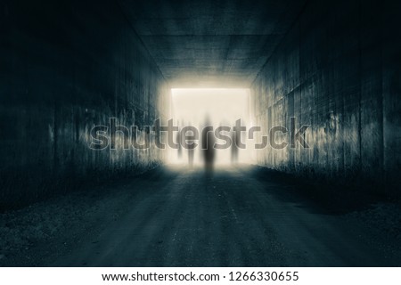 A group of ghostly figures emerging from the light at the end of a dark sinister tunnel. With a high contrast edit. Royalty-Free Stock Photo #1266330655