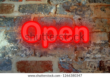 Neon lettering reading Open against worn, aged brick wall