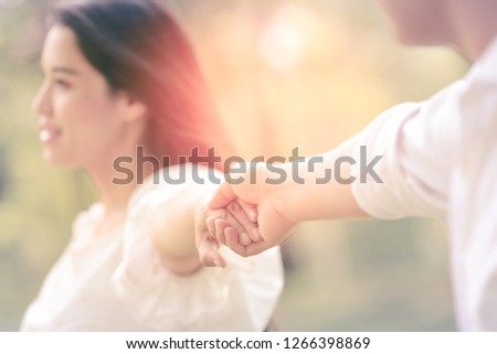 Lovers couple holding hands in a garden on summer vacation travel. Woman walking on romantic honeymoon promenade holidays holding hand of husband following her, view from behind. Focas at hand.