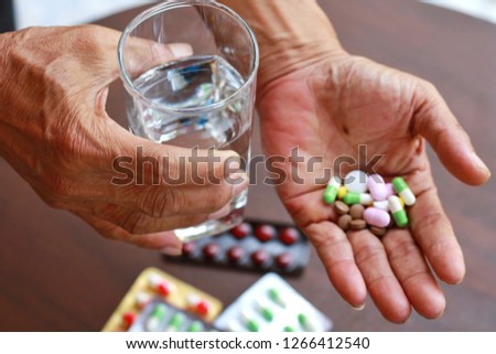 Elderly Asian man holding many pills (tablet,capsule ) and glass of water in hands.Taking a lot of medicine, supplements ,antibiotic antidepressant or painkiller medication.Hope for cure,Top view. Royalty-Free Stock Photo #1266412540