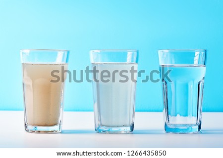 Water filters. Concept of three glasses on a white blue background. Household filtration system. Royalty-Free Stock Photo #1266435850