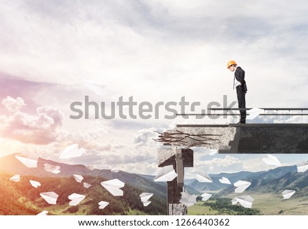 Young engineer in suit and helmet looking down while standing among flying paper planes on broken bridge with skyscape and nature view on background. 3D rendering.