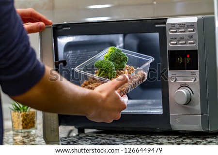 Using the microwave oven to heat food. Woman's hand puts plastic container with broccoli and buckwheat in the microwave Royalty-Free Stock Photo #1266449479