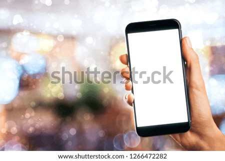 Hand holding empty white cellphone on abstract blurry christmas interior background. Holiday present device mockup concept