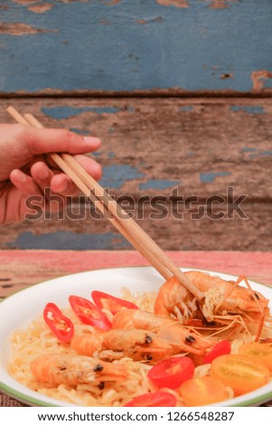 Chopsticks hold a prawn on the background of instant  noodles.  Close-up