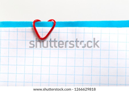 Empty sheet of checkered paper on a clip in the form of a heart. Blank for Valentine Day Love Card, blue background