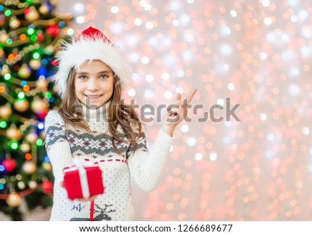 Smiling girl holding  gift box and pointing away. Empty space for text