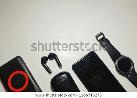 45 degree flatlay picture of black wireless charging powerbank, twin wireless earphone, smart watch and smartphone.