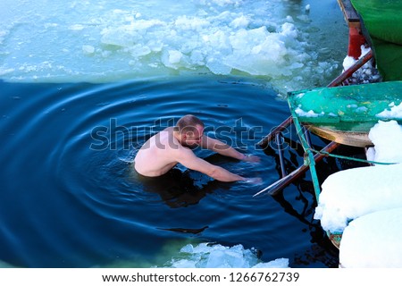 A young man descends into the ice hole. Russian winter swimming. Cold hardening of the body.