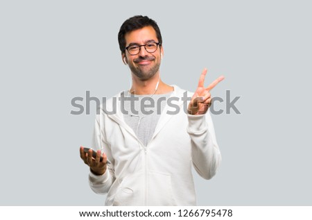 Man with glasses and listening music smiling and showing victory sign with a cheerful face on grey background