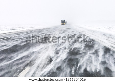 Traffic on highway in snow blizzard. Cars on snowy asphalt road drives in dangerous conditions with bad visibility and strong wind Royalty-Free Stock Photo #1266804016