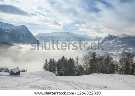 Alps in winter. Mountain peaks in the fog.  The sun's rays Shine through the mountain tops. Volumetric clouds in the blue winter sky