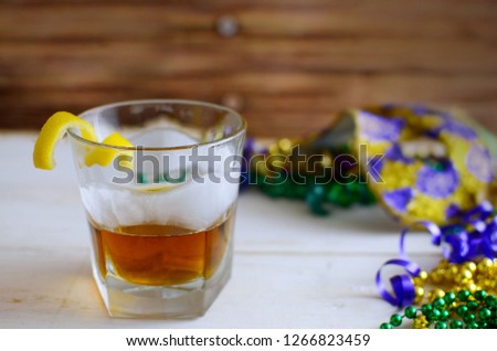 A sazerac cocktail with a lemon twist in a rocks glass on a wooden table. Mardi gras decorations around. Wooden background.